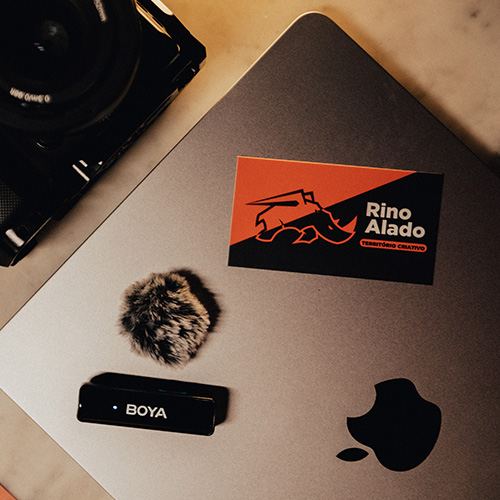 Cartão de visita da Rino Alado sobre mesa de trabalho com equipamentos de produção